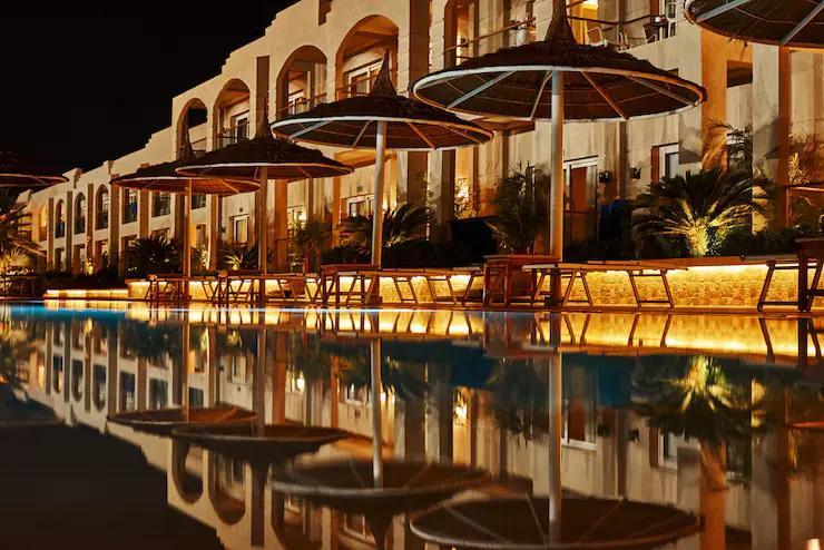 Luxurious resort complex featuring traditional Moroccan architectural design with dramatic evening lighting reflected in pristine pool waters, representing the upscale accommodations and enchanting ambiance found at all inclusive resorts in Morocco