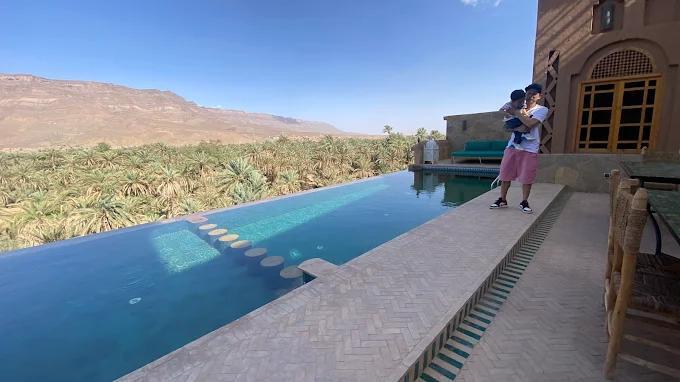 Scenic infinity pool overlooking palm groves and mountains at one of the best resorts in Morocco, with a man holding a child by the poolside.
