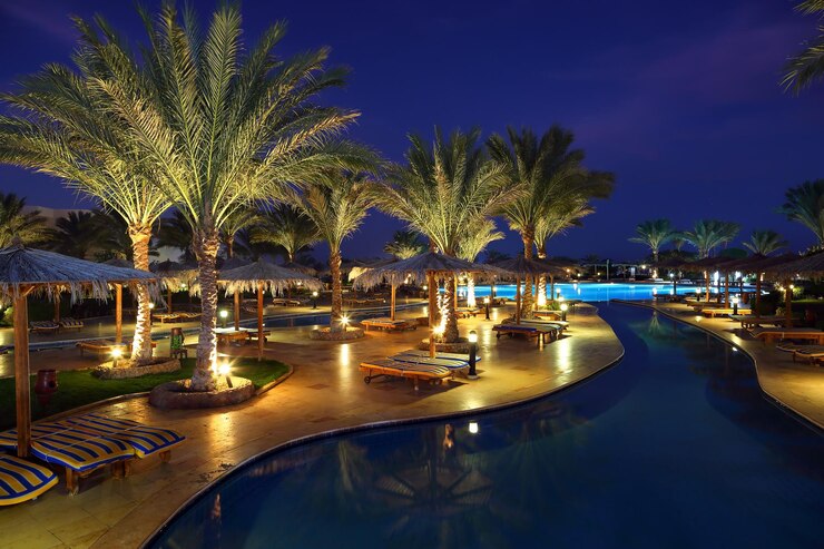 Luxurious resort poolside illuminated at night with palm trees and elegant lounge areas, showcasing the upscale accommodations offered in Morocco Travel Packages.