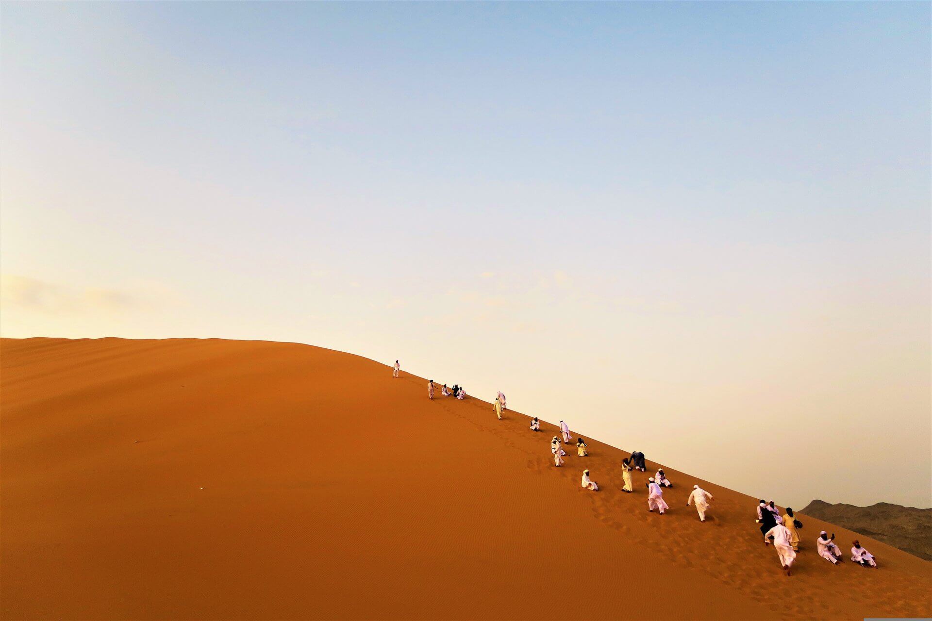 Visit Morocco: A Luxury Journey Through Imperial Cities, Atlas Peaks and Sahara Dunes 10 Group of visitors climbing a towering orange sand dune in the Moroccan Sahara at dusk, best experienced October through April